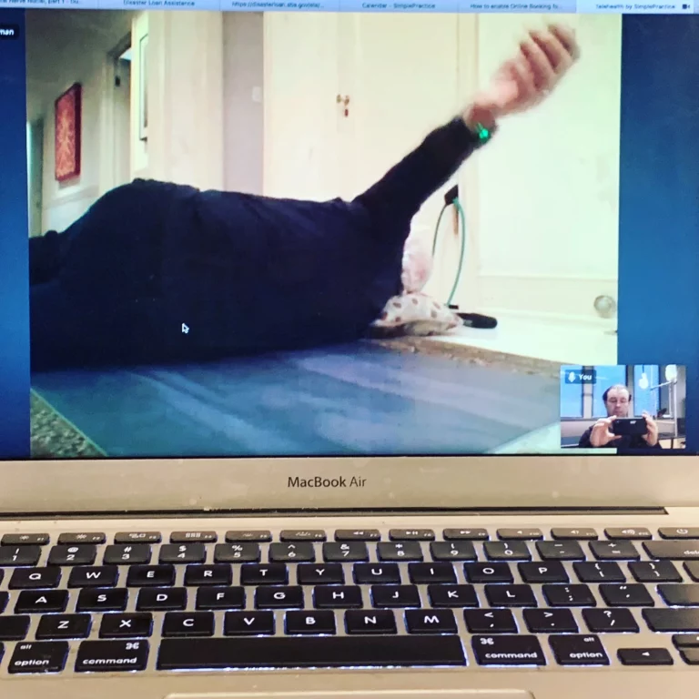 A video call on a laptop shows one person lying on an exercise mat with their arm raised and another person visible in a small video window.