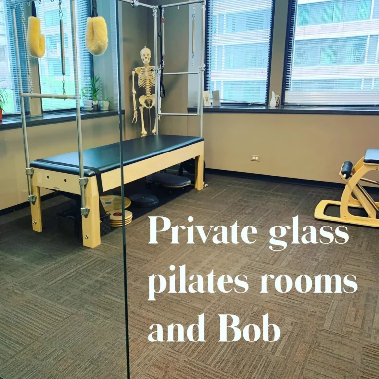 A pilates studio room with exercise equipment, large windows, and a human skeleton model in the corner. Text on the glass reads, "Private glass pilates rooms and Bob.
