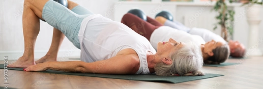 Three older adults lie on yoga mats indoors, performing a glute bridge exercise during one of the Small Group Fitness Classes in Chicago.